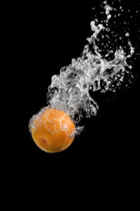 grapefruit falling into water and living a trail of water and droplets. perfect capture against black backdrops