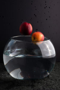 scenario for water splash photo. glass aquarium with water, black backdrops. apples or nectarines fruits still in the air going into aquarium direction