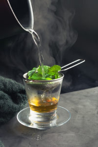 fresh mint cup of tea. boiling water being poured in the cup with steam, a wool blanket and dark background. side light